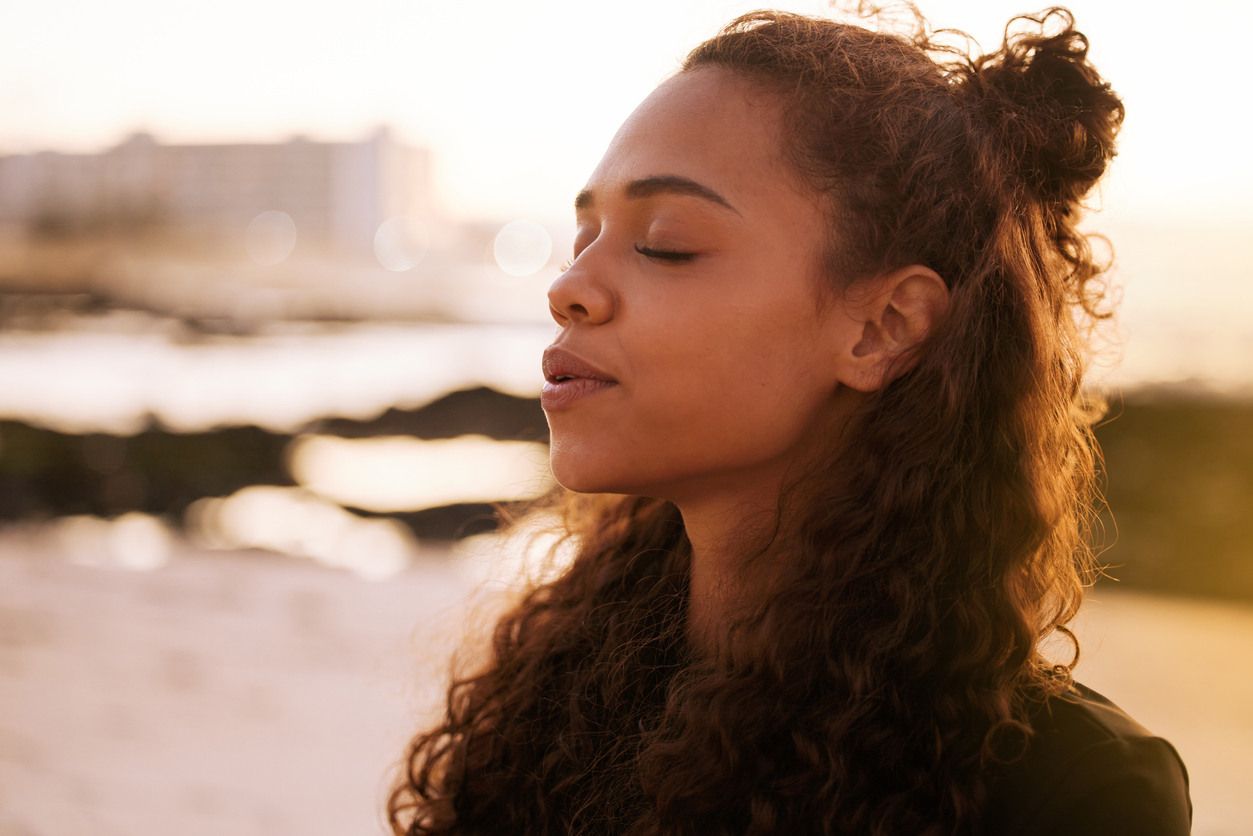 A woman breathes deeply on a sunlit beach.
